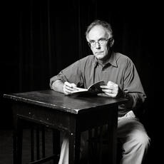 A black and white image of Tomaz Salamun sitting at a desk with a book open
